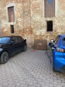 Due auto collegate a un punto di ricarica davanti a un edificio in pietra.