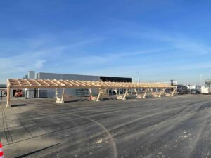 Pensilina fotovoltaica in legno in costruzione su un parcheggio in cemento.