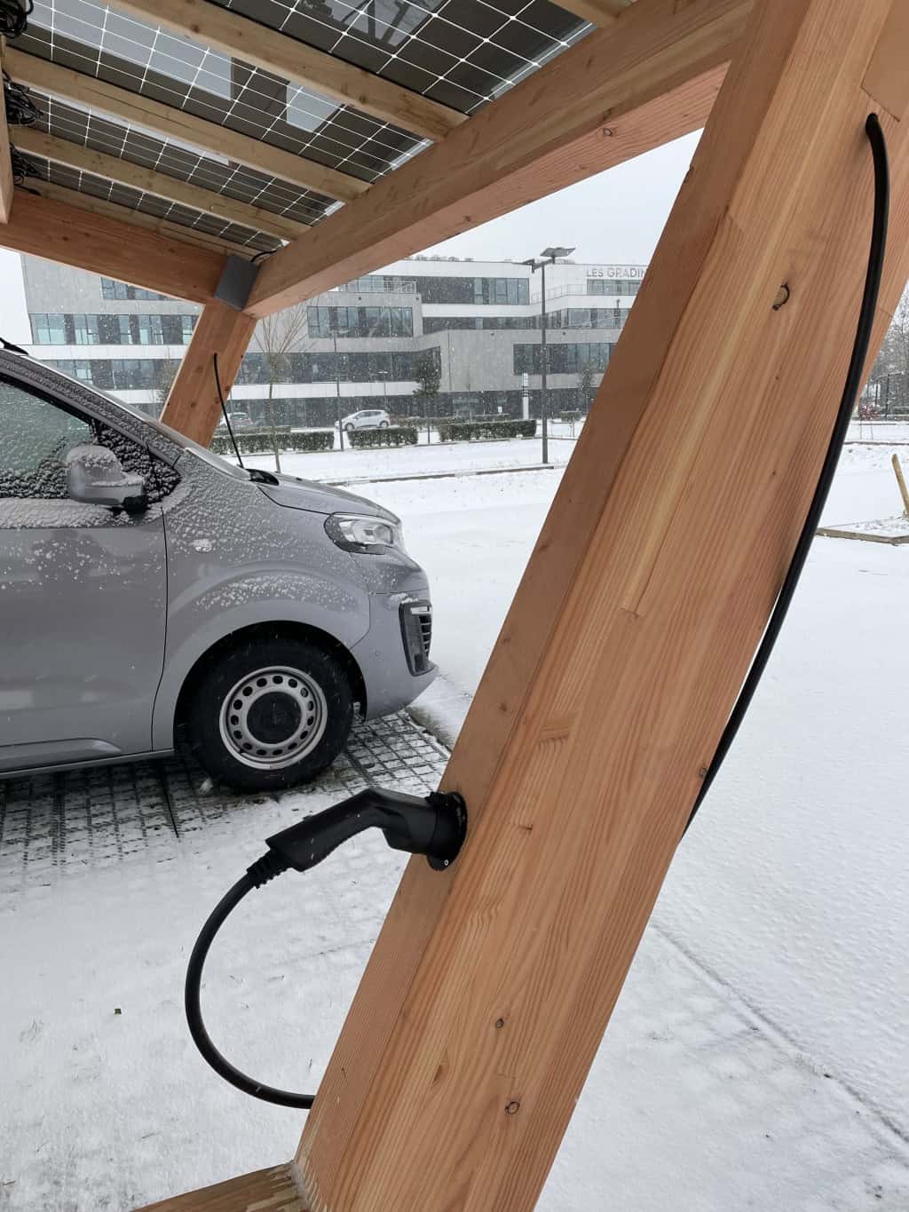 Un'auto in carica sotto un'ombra fotovoltaica coperta di neve.