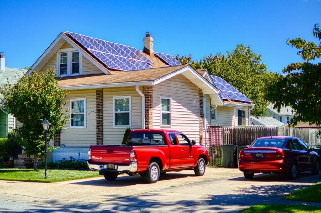 Una casa con pannelli fotovoltaici sul tetto e due auto rosse parcheggiate davanti.