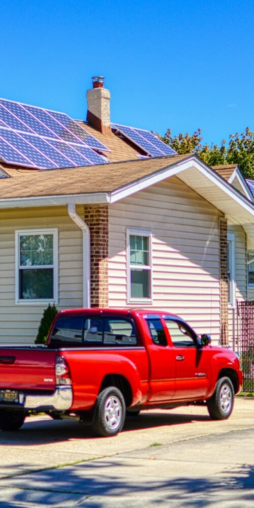 Una casa con pannelli fotovoltaici sul tetto e due auto rosse parcheggiate davanti.